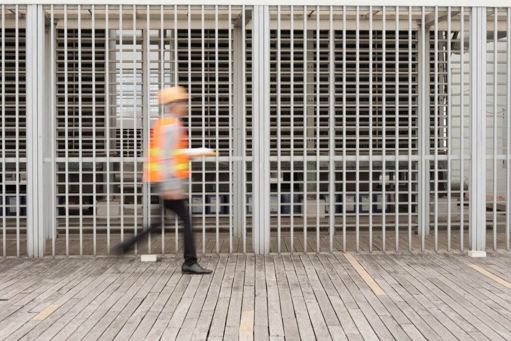 Worker in high-visibility vest walking briskly past a metal barrier at a San Francisco construction site, motion blur conveying speed.
