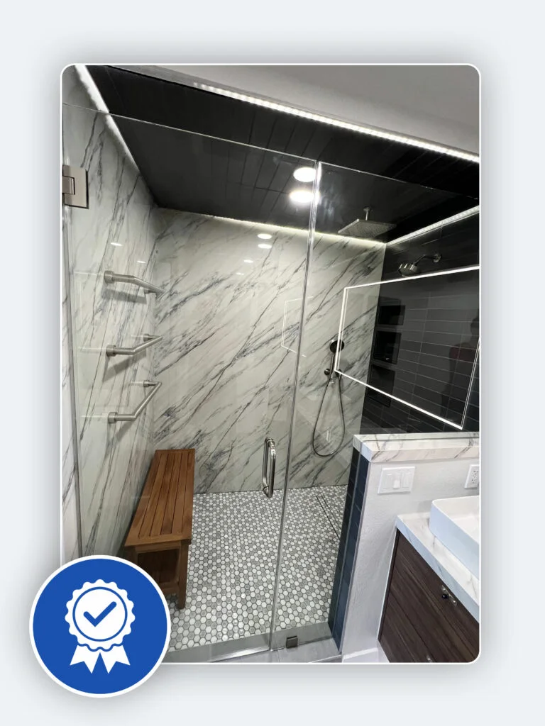 Modern bathroom remodel with glass shower enclosure, marble walls, and wooden bench.